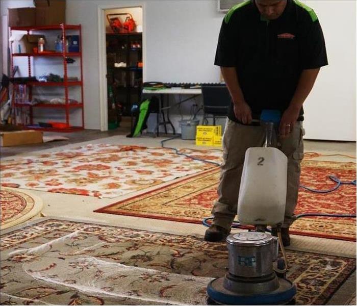 employee using a carpet cleaner to clean rugs laid out on the floor